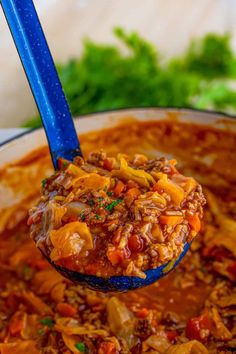 a ladle full of chili and beans is being held up by a blue spoon