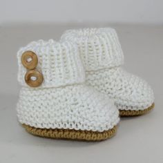 a pair of white knitted baby boots with wooden buttons on the front and bottom