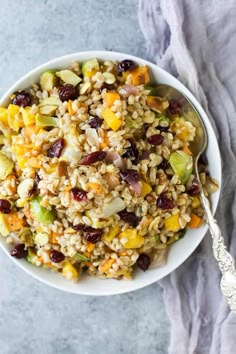 a bowl filled with rice and vegetables on top of a blue table cloth next to a spoon