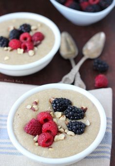 two bowls filled with oatmeal and berries on top of a table next to spoons