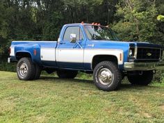 a blue and white pickup truck parked on top of a grass covered field next to trees