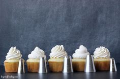 five cupcakes with white frosting and silver cones