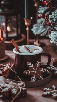 a cup of hot chocolate and cinnamon sticks on a plate next to some christmas decorations