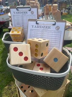 several wooden dices are stacked in a bucket on the grass, with two signs attached to them