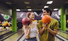 a man and woman holding up two large balls in an indoor bowling alley, smiling at each other