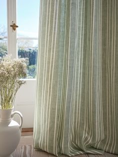 a vase with flowers in it sitting next to a window sill near a curtain