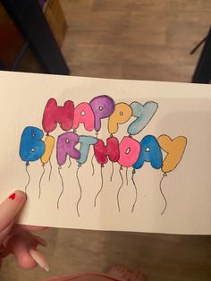 someone holding up a card with the words happy birthday written in colorful balloons on it