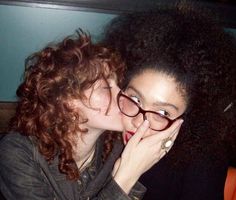 two women with curly hair are kissing each other while sitting down on a couch together