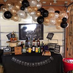 a birthday party with balloons, bottles and liquors on a table in front of a sign that says happy birthday