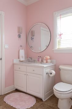 a white toilet sitting next to a bathroom sink under a round mirror on a pink wall