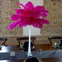 there is a tall vase with pink feathers on it at the center of this table