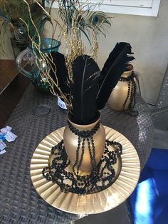 a decorative vase with black feathers and beads on a table next to a potted plant