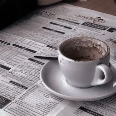 a coffee cup sitting on top of a white saucer next to a pile of newspapers