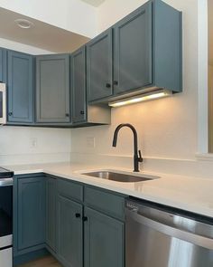 an empty kitchen with blue cabinets and white counter tops, stainless steel dishwasher