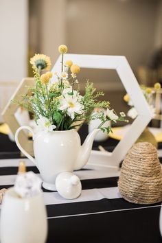 a white tea pot filled with flowers on top of a black and white table cloth