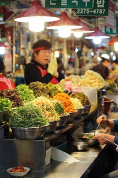 people are standing in line at a food stand with many different types of foods on display