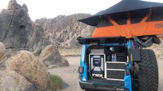 an orange and black tent on the back of a blue truck with rocks in the background