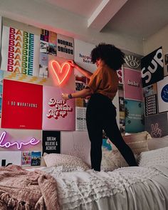 a woman standing on top of a bed next to a wall with posters and neon lights