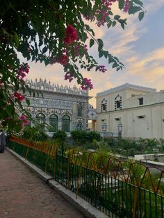 the building is white and has pink flowers on it's front fence, along with other buildings in the background