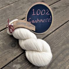 two skeins of white yarn sitting on top of a wooden table next to a sign