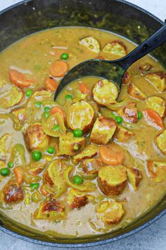 a pot filled with stew and vegetables on top of a counter next to a wooden spoon