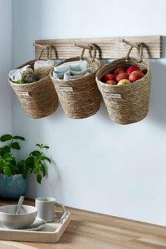 three baskets hanging on the wall with apples and other fruit in them next to a bowl