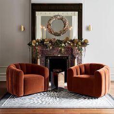 two orange chairs sitting in front of a fireplace with a wreath on the mantel