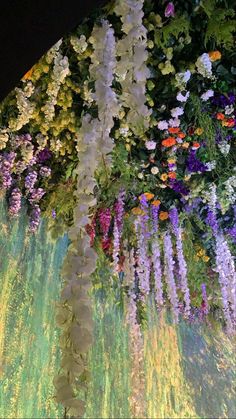 a large display of flowers hanging from the side of a building at night with lights on it