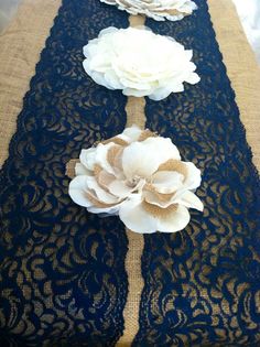 the table runner is decorated with white flowers on black lace and burlap ribbon