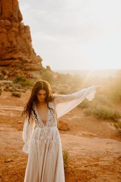 a woman standing in the desert with her arms spread out and wearing a white dress