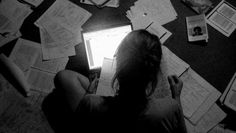 a woman is sitting on the floor with papers all over her and looking at a laptop