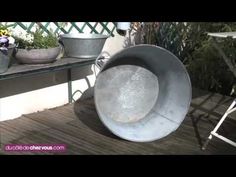 a metal object sitting on top of a wooden deck next to potted plants and flowers