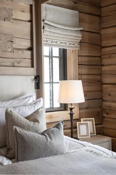 a bedroom with wooden walls and white linens on the bed in front of a window