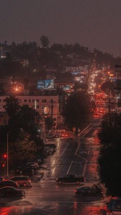 a city street at night with cars driving on the road and buildings in the background