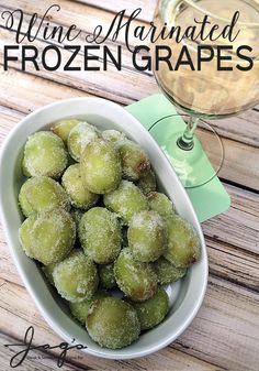 a white bowl filled with frozen grapes next to a glass of wine on top of a wooden table