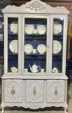 a white china cabinet with glass doors and gold trimmings on the bottom shelf