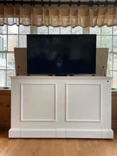 a flat screen tv sitting on top of a white cabinet in front of a window