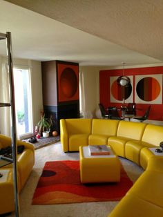 a living room filled with yellow furniture next to a red and black wall mounted painting