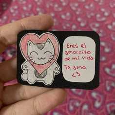 a hand holding a small sticker with a drawing of a cat in the shape of a heart