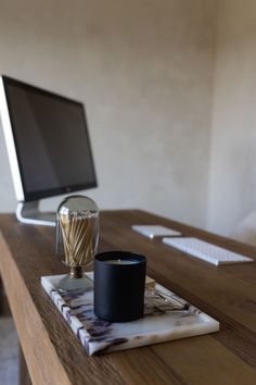 a wooden desk topped with a computer monitor next to a cup and candle on top of it