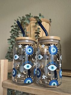 two mason jars decorated with blue and white evil eye designs on top of a wooden shelf