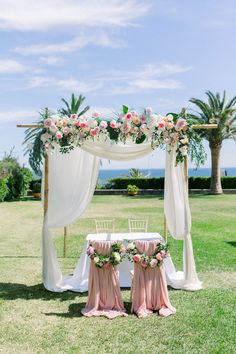 an outdoor wedding setup with white drapes, pink flowers and greenery on the table