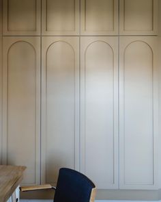 a chair sitting on top of a wooden table in front of white cupboards with arched doors