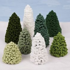 crocheted christmas trees are lined up in rows on a white surface with blue sky in the background