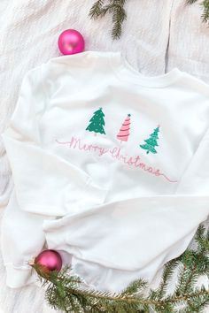 a white sweatshirt with merry christmas trees on it and pink ornaments around the sweaters