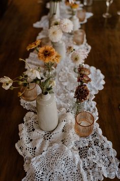 the table is covered with white doily and decorated with vases filled with flowers