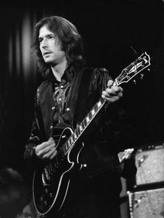 a man playing an electric guitar while wearing a leather vest and looking at the camera