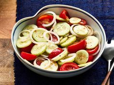 a bowl filled with cucumbers and tomatoes on top of a blue place mat