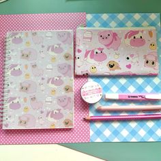 a pink notebook and pen sitting on top of a blue checkered tablecloth covered desk