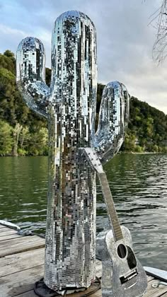 a metal cactus with a guitar sitting on top of it's head in front of the water